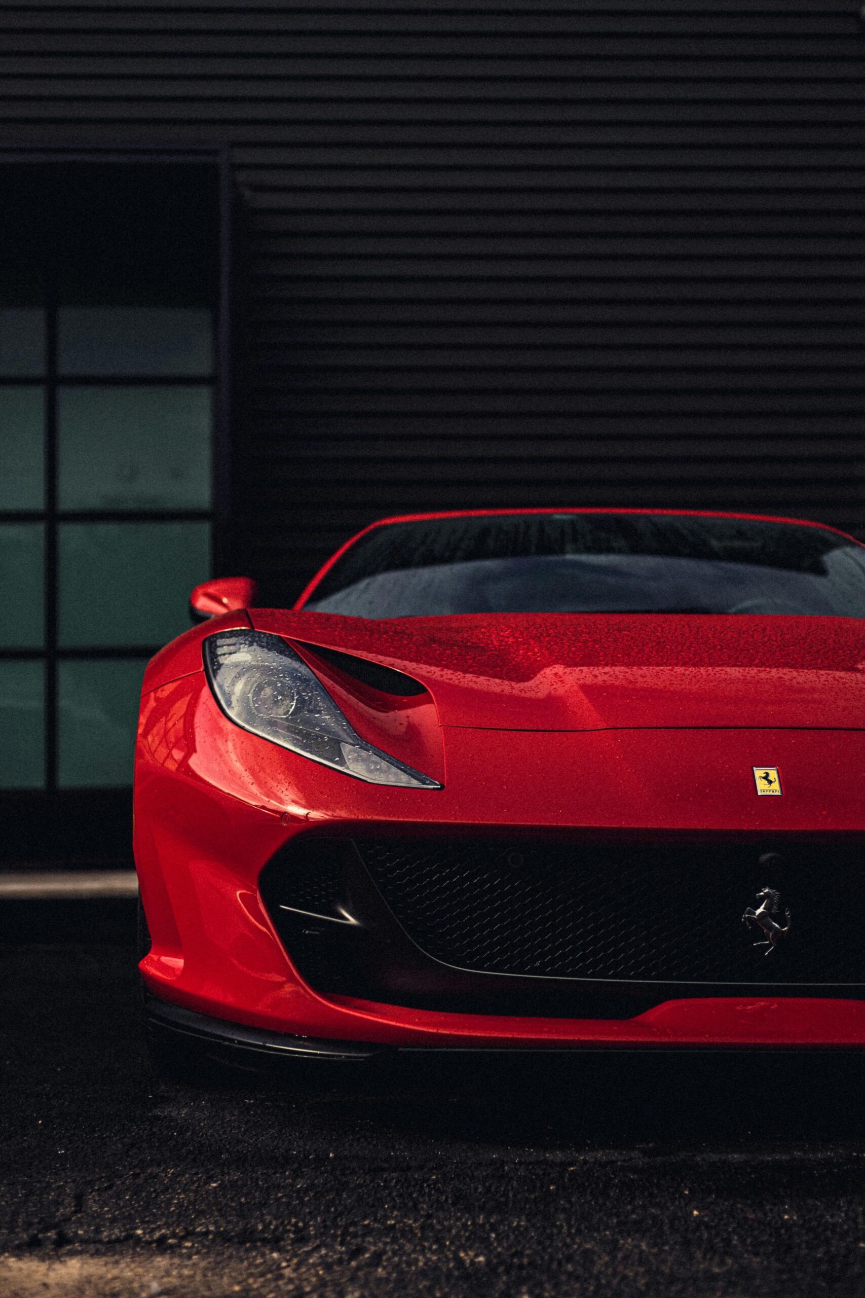 Front view of a luxury red Ferrari sports car with water droplets parked outdoors.